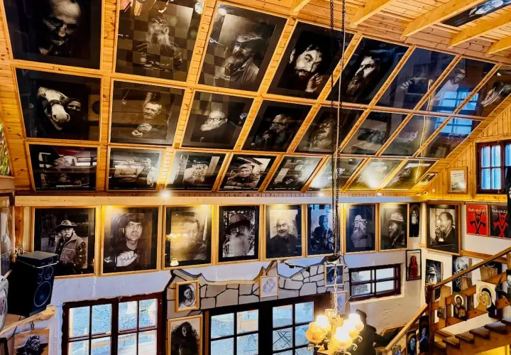 Wnętrze z licznymi czarno-białymi portretami, tworzącymi siekierozada cisna historia. Drewniane ściany i sufit podkreślają artystyczny klimat.