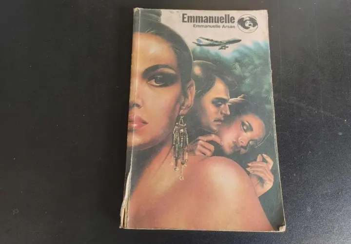 Okładka książki "Emmanuelle" z wizerunkiem kobiety i pary, w tle samolot i dżungla.