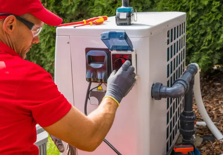 Technik w rękawiczkach sprawdza panel pompy ciepła, by zapewnić optymalną, jaką temperaturę daje pompa ciepła. Narzędzia leżą obok.