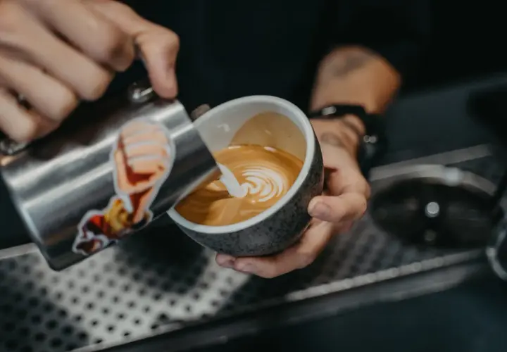 Barista tworzy wzorek na kawie, nalewając spienione mleko. To prosty sposób, jak zrobić wzorek na kawie.