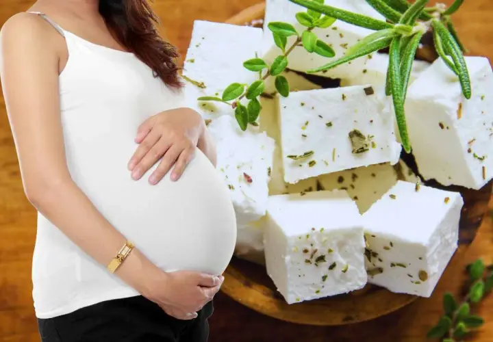 Pancia di donna incinta accarezzata, con cubetti di feta aromatizzata alle erbe sullo sfondo.