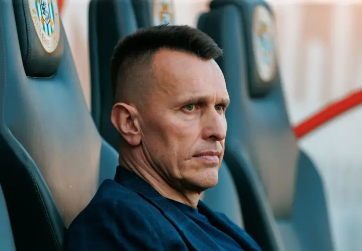 Skupiony trener Zagłębia Lubin siedzi na ławce rezerwowych, analizując grę.