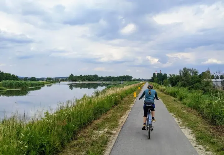 Kobieta na rowerze przemierza ścieżkę nad wodą, ciesząc się pięknem przyrody. To idealne miejsce na **velo Skawina**.