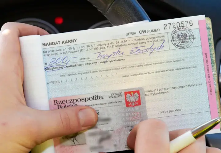 Mandat karny na 300 zł za wykroczenie. W tle widać fragment deski rozdzielczej samochodu, sugerujący, że zdarzenie miało miejsce na skrzyżowaniu.