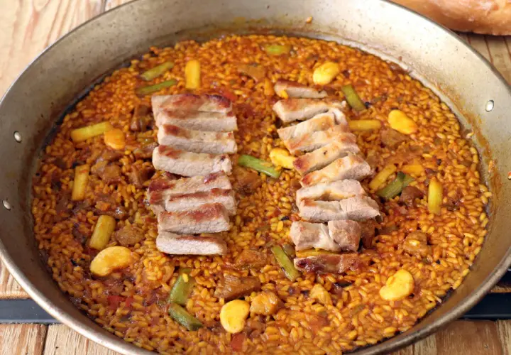 Arroz con secreto de cerdo, jugoso y dorado, con trozos de carne y verduras en una paellera.
