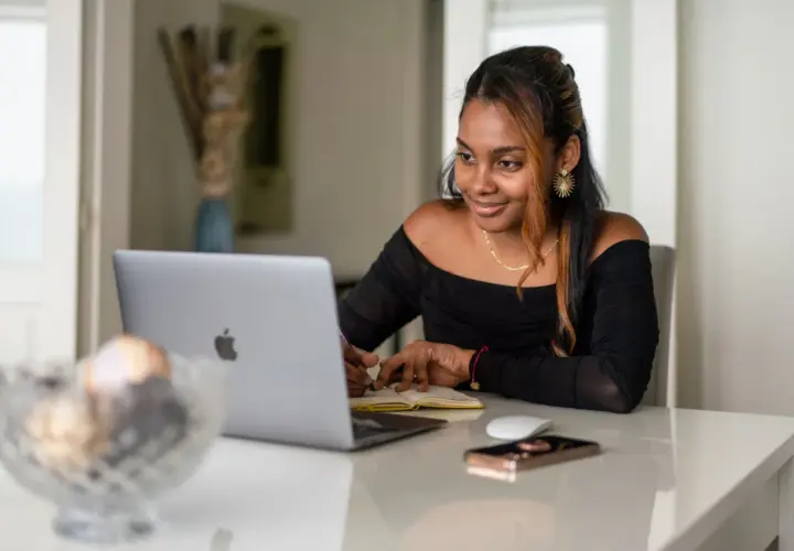 Giovane donna sorride mentre studia o lavora al computer, forse per insegnare inglese online.