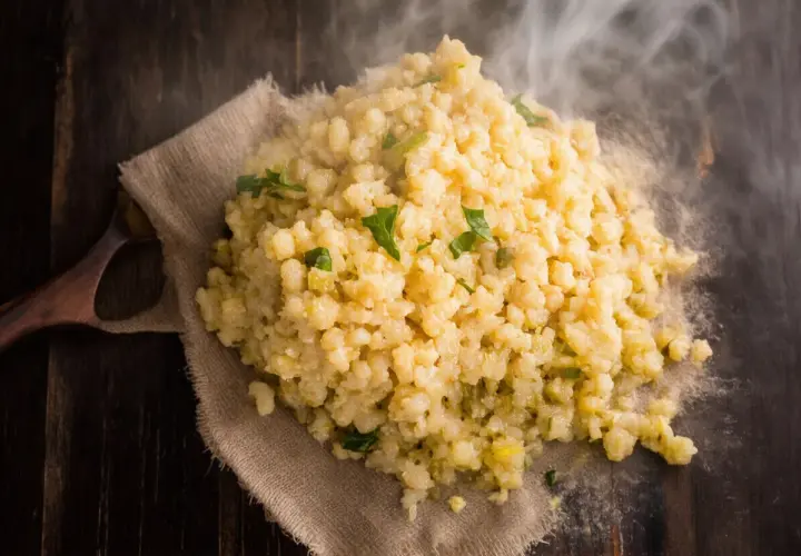 Gorąca kasza bulgur gotowanie na drewnianym stole, parująca i ozdobiona zielonymi ziołami.