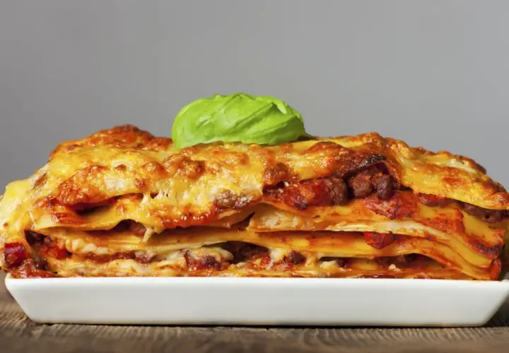 Una porción generosa de lasagna italiana, con capas de pasta, carne y queso derretido, coronada con una hoja de albahaca fresca.