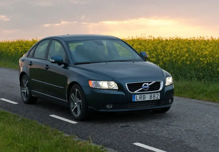 Ciemnozielone Volvo S40 2.0 diesel jedzie wiejską drogą pośród kwitnącego rzepaku.