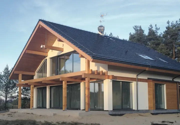 Nowoczesny dom z gotowych elementów, z drewnianą konstrukcją i dużymi przeszkleniami, otoczony lasem.