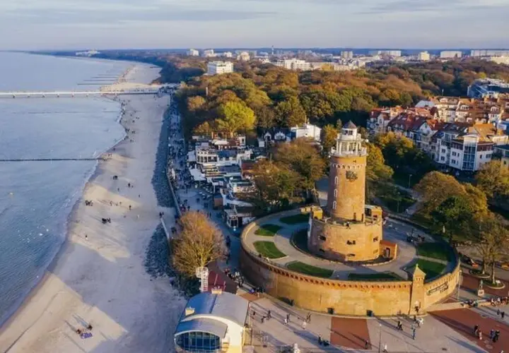 Widok na latarnie morskie w Polsce, z charakterystyczną wieżą w Kołobrzegu, plażą i morzem.