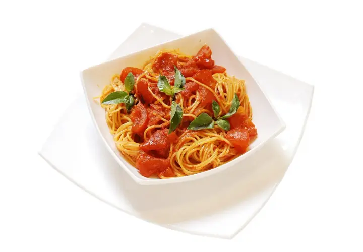Un invitante piatto di spaghetti al pomodoro fresco, guarnito con foglie di basilico verde brillante, pronto per essere gustato.
