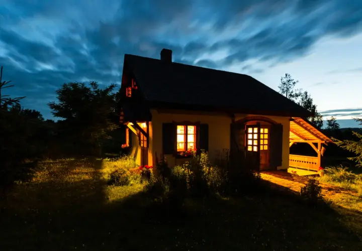 Przytulny domek na cisowym wzgórzu, oświetlony ciepłym światłem z okien, na tle rozmytego, granatowego nieba.