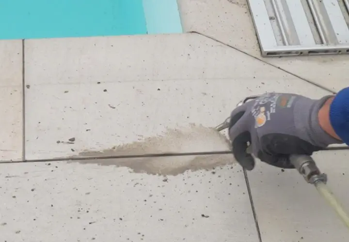 Arbeiter erneuert mit Sprühpistole die Silikonfugen auf gefliestem Boden neben einem Pool.