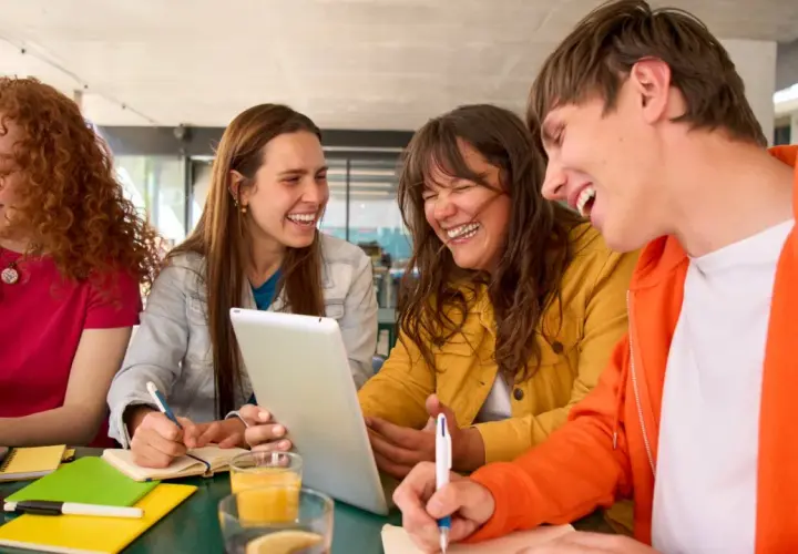 Uśmiechnięci studenci, którzy uczą się psychologii na studiach zaocznych, pracują razem przy stole, korzystając z laptopa i tabletu.