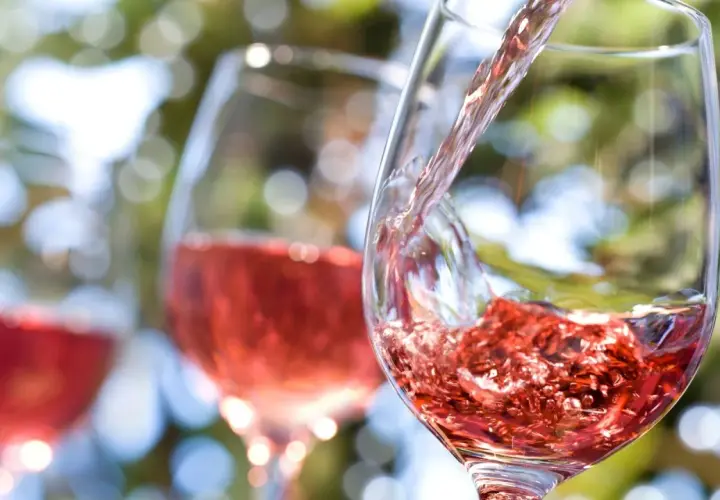 Vin rosé versé dans un verre, avec d'autres verres en arrière-plan flou.