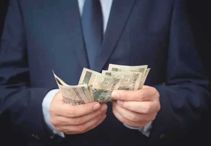 Mężczyzna w garniturze liczy banknoty. Może to symbolizować otrzymanie odszkodowania i zadośćuczynienia po trudnym zdarzeniu.