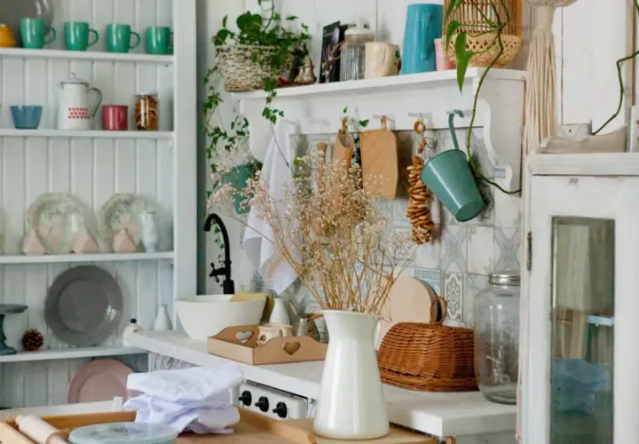 A cozy granny chic kitchen with shelves full of colorful mugs, plates, and jars. A bouquet of dried flowers adds a rustic touch.