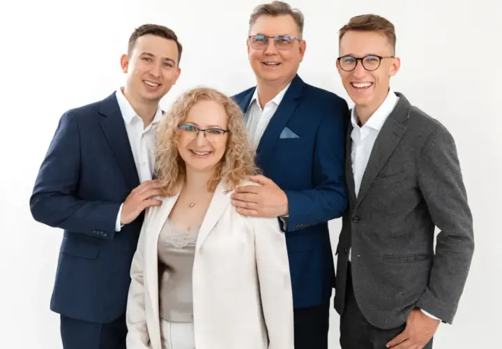 Cztery osoby w eleganckich strojach, uśmiechnięte, na białym tle.