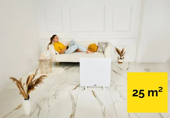 Kobieta relaksuje się na kanapie, podczas gdy grzejnik na podczerwień ogrzewa pomieszczenie o powierzchni 25 m².