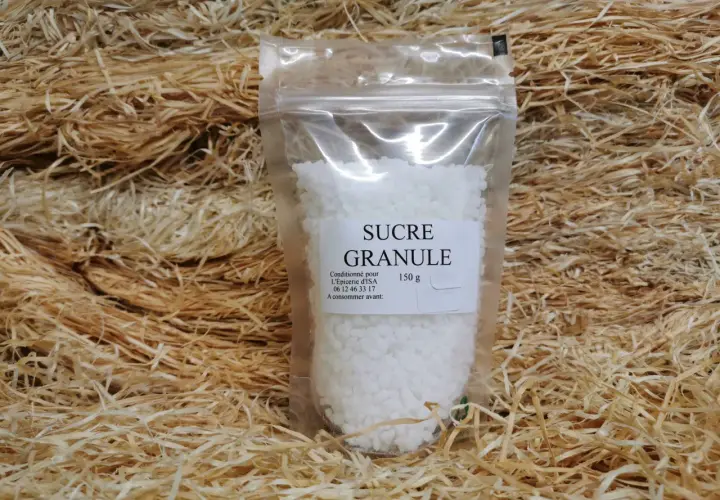 Un sachet de sucre granulé, 150g, est présenté sur un lit de copeaux de bois. Ce sucre granulé, c'est quoi ? C'est du sucre cristallisé.