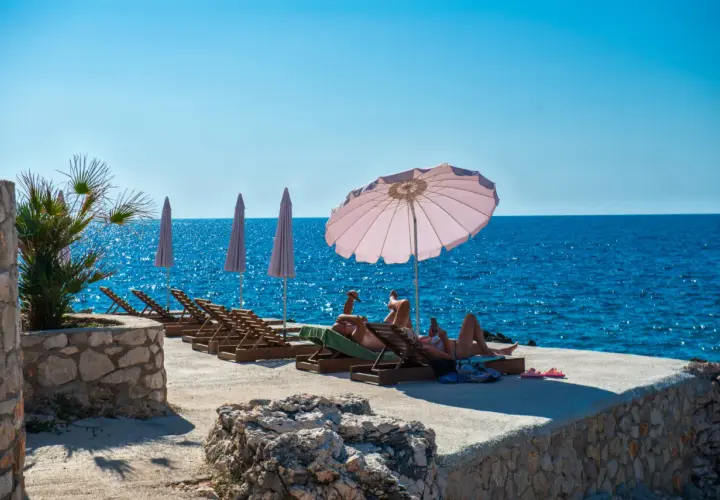 Relaks na plaży w Czarnogórze. Czy czarnogóra jest bezpieczna? Turyści odpoczywają na leżakach przy turkusowym morzu.