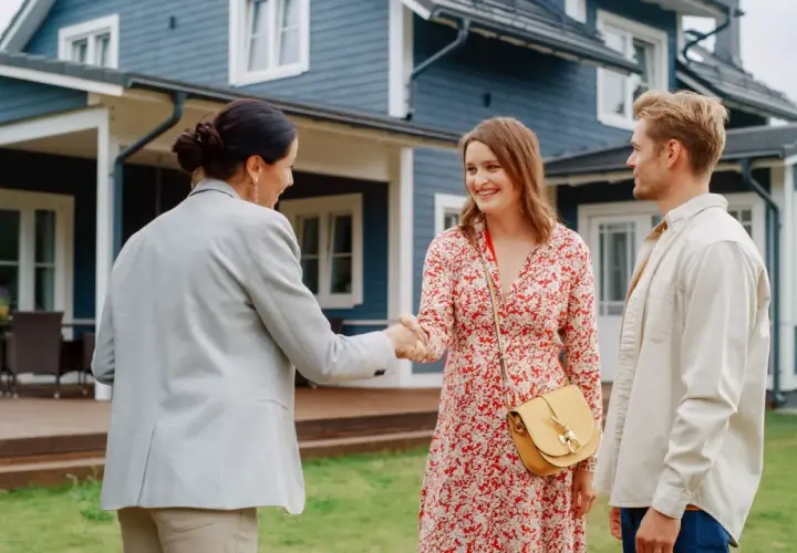 Un couple heureux serre la main d'une agente immobilière devant leur nouvelle maison. Ils ont réussi à vendre leur ancienne propriété et à garder leur prêt.