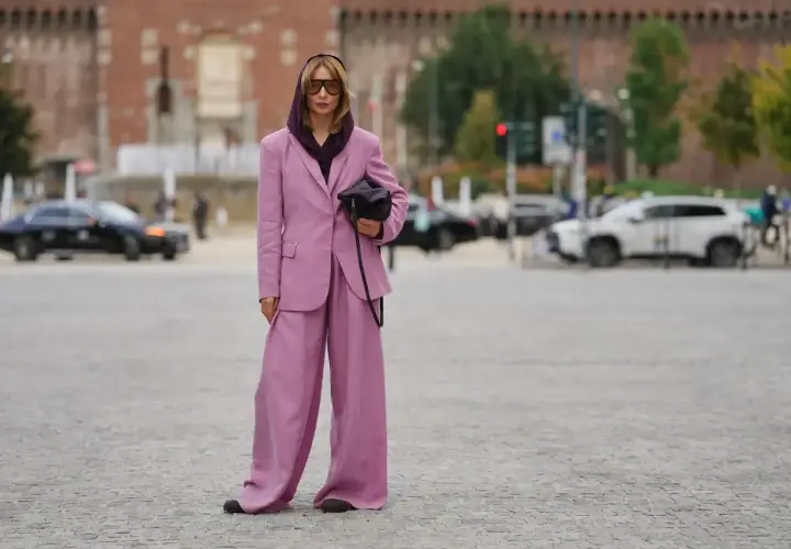 Kobieta w garniturze w kolorze mauve, z szerokimi nogawkami spodni, pozuje na tle miasta.