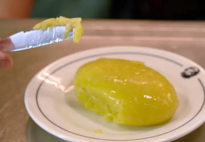 Un cuchillo recoge una porción de cremoso alioli casero, listo para untar sobre un plato blanco.