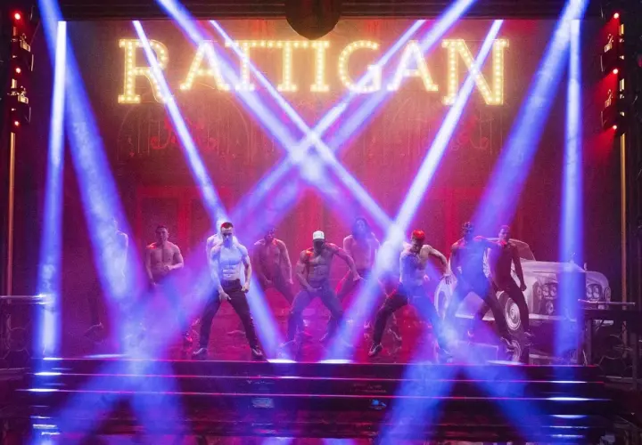 Mężczyźni tańczą na scenie w świetle niebieskich reflektorów, pod neonowym napisem "RATTIGAN". To scena z filmu Magic Mike 1.