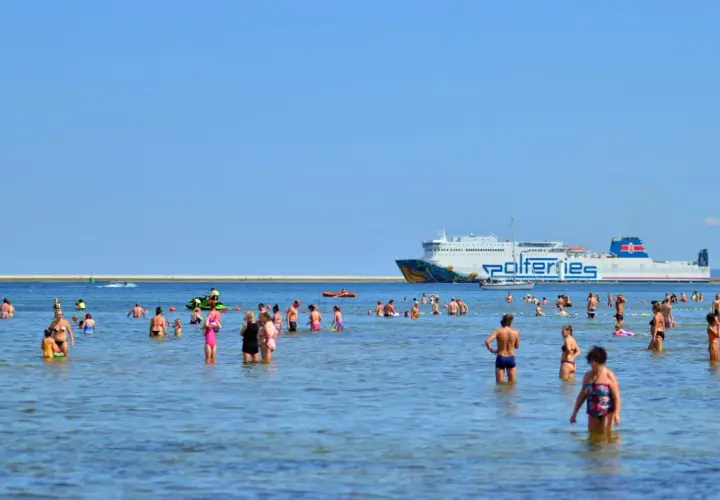 Ludzie kąpią się w morzu, a w tle widać prom Polferries. Szukasz informacji o prom Świnoujście-Ystad cena?