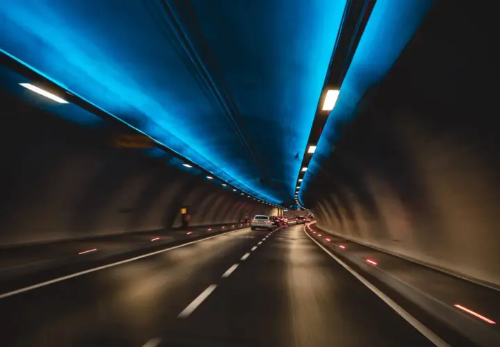 Jadące samochody w tunelu drogowym z niebieskim oświetleniem sufitowym.