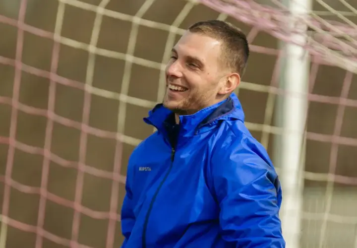 Uśmiechnięty piłkarz w niebieskiej kurtce, gotowy do gry w stylu tiki-taka.