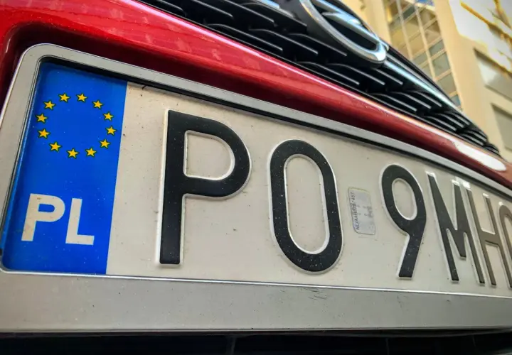 Czerwony samochód z polską tablicą rejestracyjną PO 9MH0. Widoczny fragment grilla i logo marki.