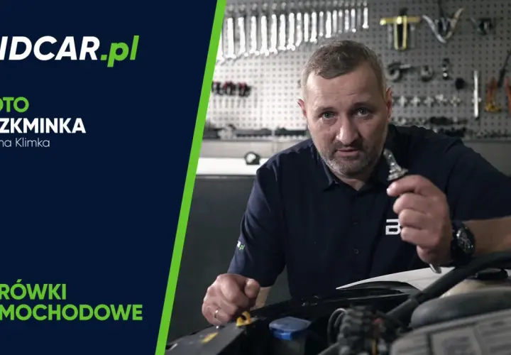 Mężczyzna pokazuje żarówkę samochodową, przygotowując się do jej wymiany. W tle warsztat z narzędziami.