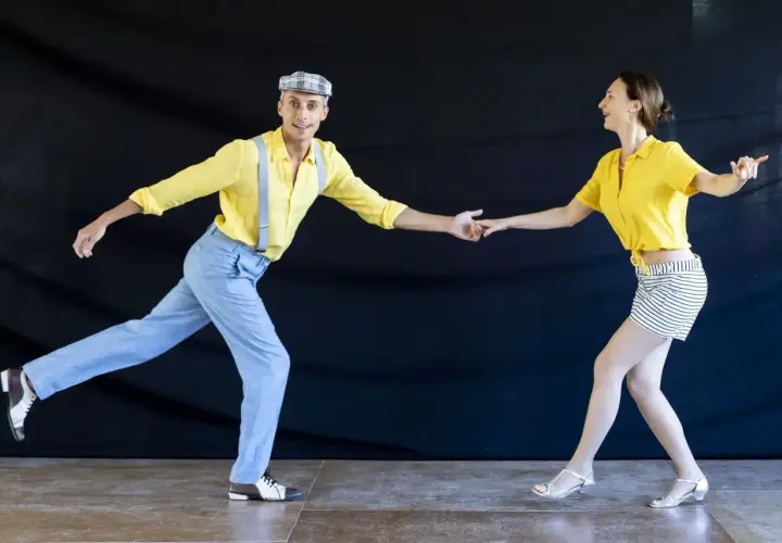 Coppia in abiti vintage che esegue un energico lindy hop ballo, con lui in giallo e bretelle, lei in giallo e gonna a righe.