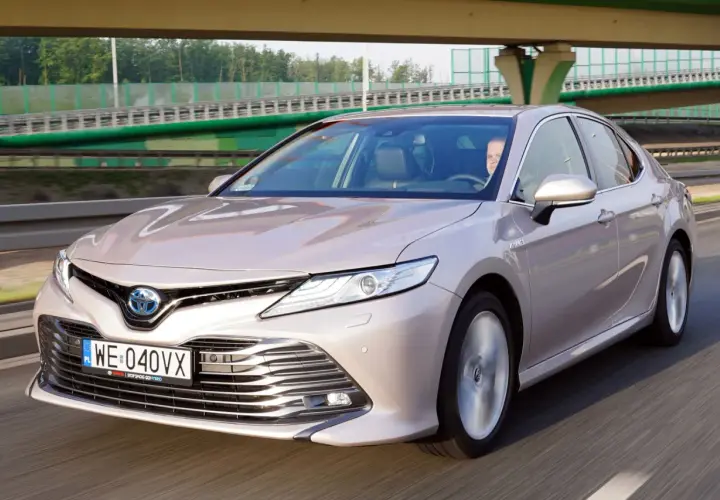 Elegancka, beżowa Toyota Camry 2023 na drodze, z kierowcą za kierownicą.