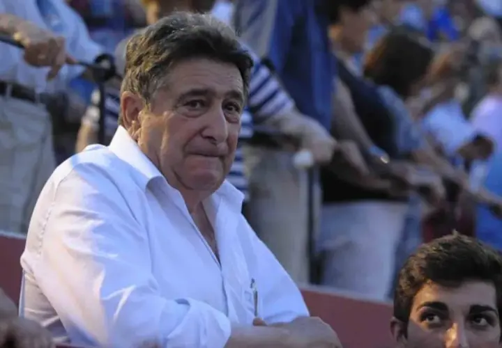 Hombre mayor con camisa blanca, posible dueño de ganadería Domingo Hernández, observa atentamente en una plaza de toros.