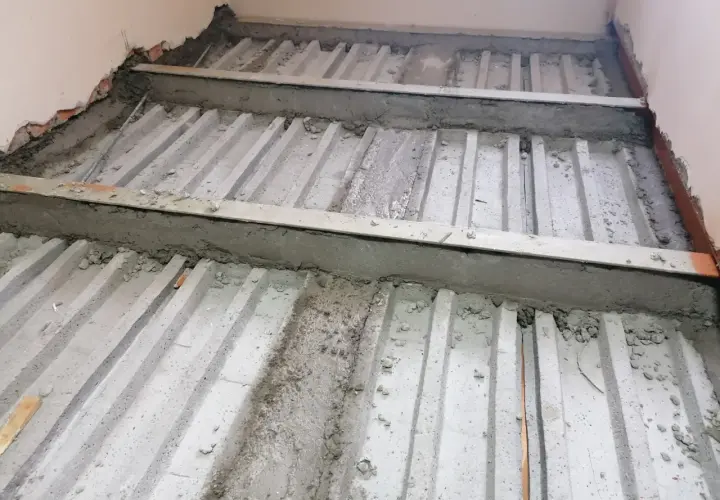 Prace nad tym, jak wzmocnić strop w starym domu. Widoczne betonowe belki i metalowe wsporniki, przygotowywane do dalszych prac budowlanych.