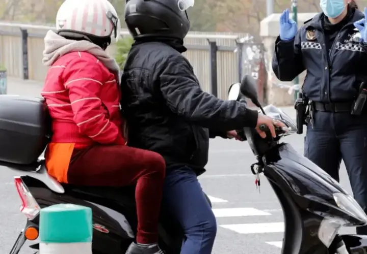 Agente de policía detiene a pareja en moto. Podrían recibir una multa por ir sin casco.