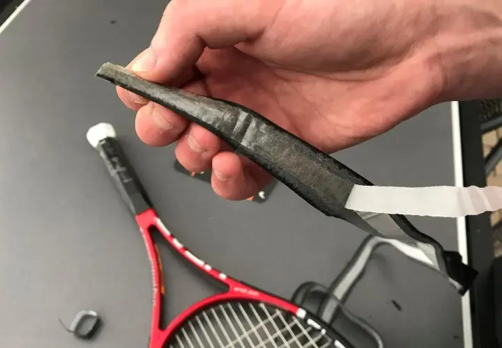 Dłoń trzyma starą, zużytą owijkę squash, która jest odklejana od rakiety.