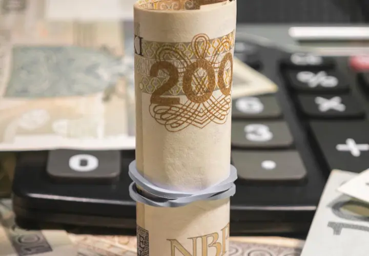 Zrolowany banknot 200 zł na kalkulatorze, obok inne nominały. Analiza millenium kurs akcji.