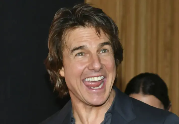 Uśmiechnięty Tom Cruise, którego twarz przypomina scenę z filmu o sekcie, z szeroko otwartymi ustami i widocznymi zębami.