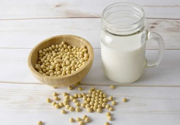Bol en bois rempli de graines de soja, à côté d'un verre de lait de soja. La lécithine de soja est un ingrédient clé.