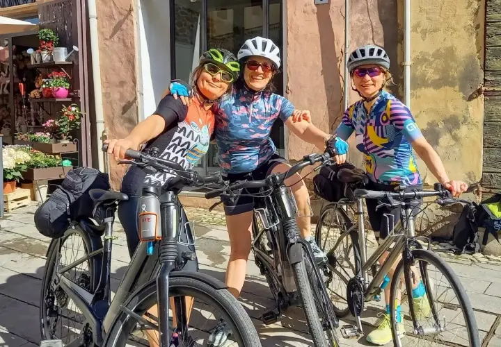 Three friends ready for guided bike tours in Europe, smiling with their bikes in front of a charming shop.