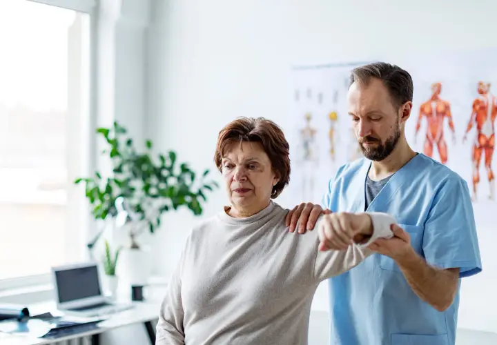 Physiotherapeut hilft einer Frau mit einer schmerzenden, verklemmten Schulter bei der Bewegung.