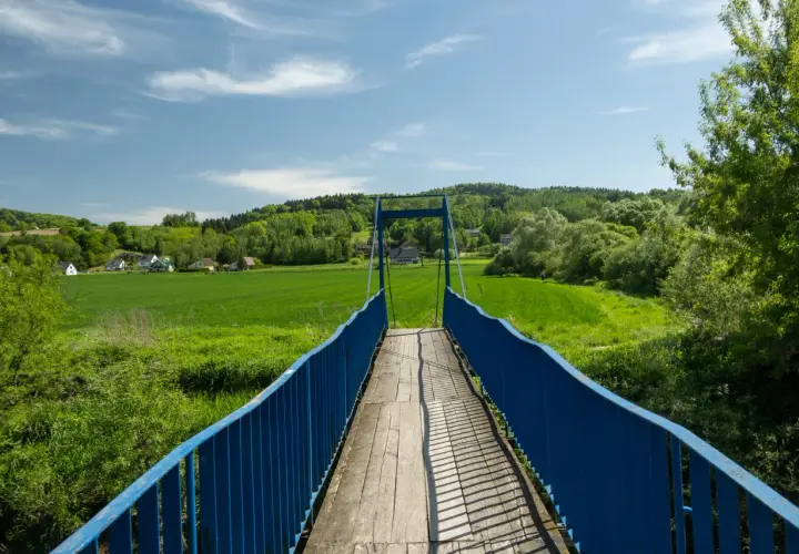 Mostek na szlaku trzech pogórzy prowadzi przez zielone pola i lasy.