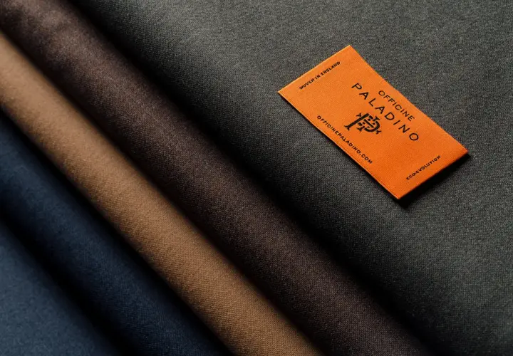A selection of different types of wool fabric in shades of blue, brown, and grey, with an orange tag from Officine Paladino.