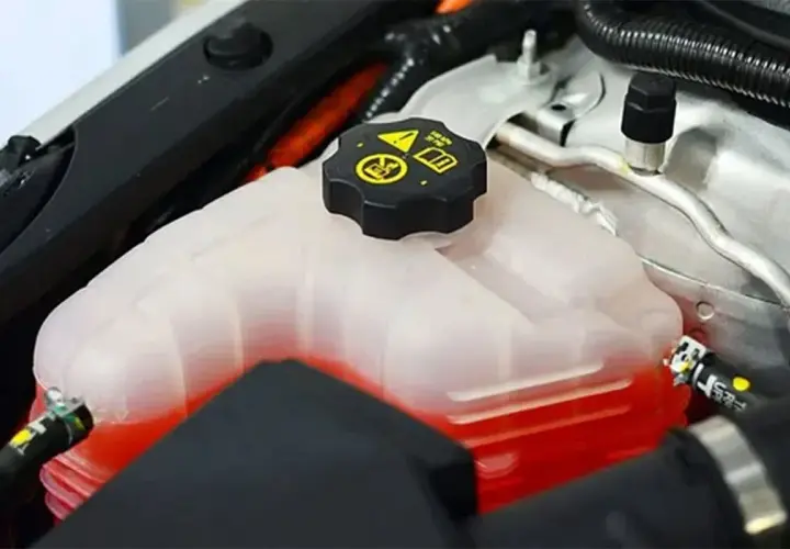 Depósito de refrigerante de coche con líquido rojo. La tapa negra tiene símbolos de advertencia. Se puede echar agua normal al coche si es necesario.