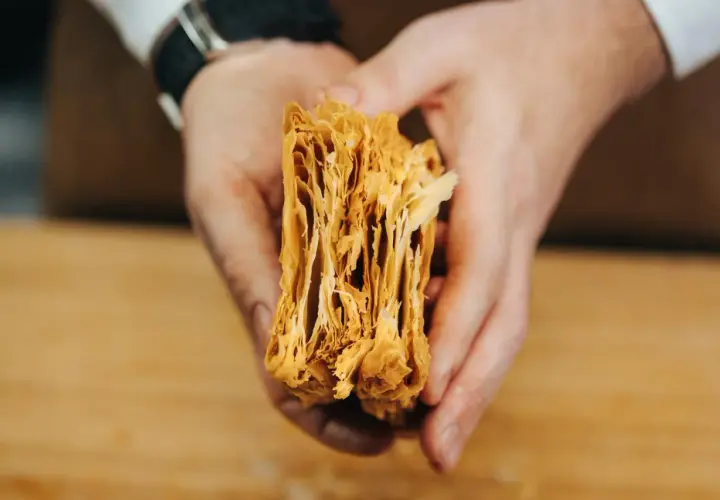 Manos sostienen un trozo de masa de hojaldre casera, mostrando sus finas y crujientes capas doradas.